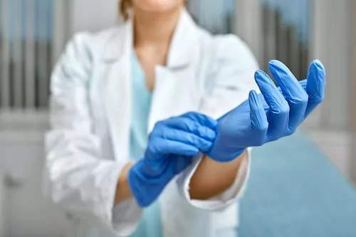 Close up of a female doctor putting a blue latex gloves on a clinic background.
