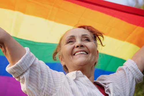 Beautiful mature senior woman with charming smile holding rainbow LGBT flag in her hands, gay and lesbian rights concept
