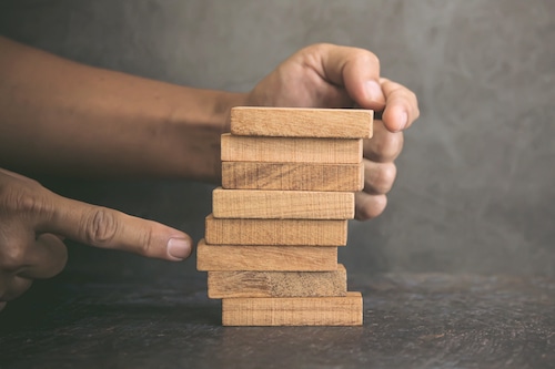 Hand prevent wooden block tower stack not crash or fall. concept of prevention of financial business and risk management or strategic planning.